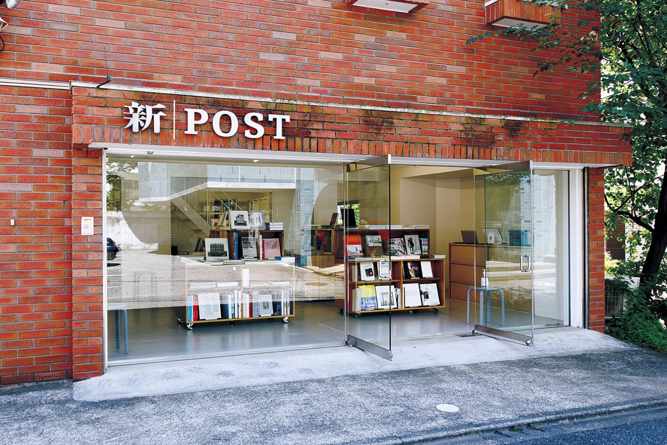 路地裏に静かに佇むタイル張りの建物の1階が書店、2階がギャラリーになっている。店名サインの「新」の文字は、湯島に新建築社の本社があった時代のものを転用し、田中義久氏がデザイン。