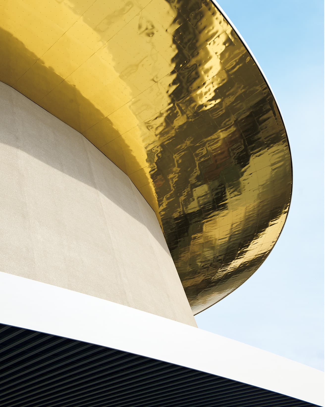 目の粗い吹き付け仕上げの白い壁と、金色に輝く屋根が〈太陽の塔〉を連想させる。軒天の仕上げは、偶然にも〈太陽の塔〉の黄金の顔の部分に現在使われているものと同じ製品だという。