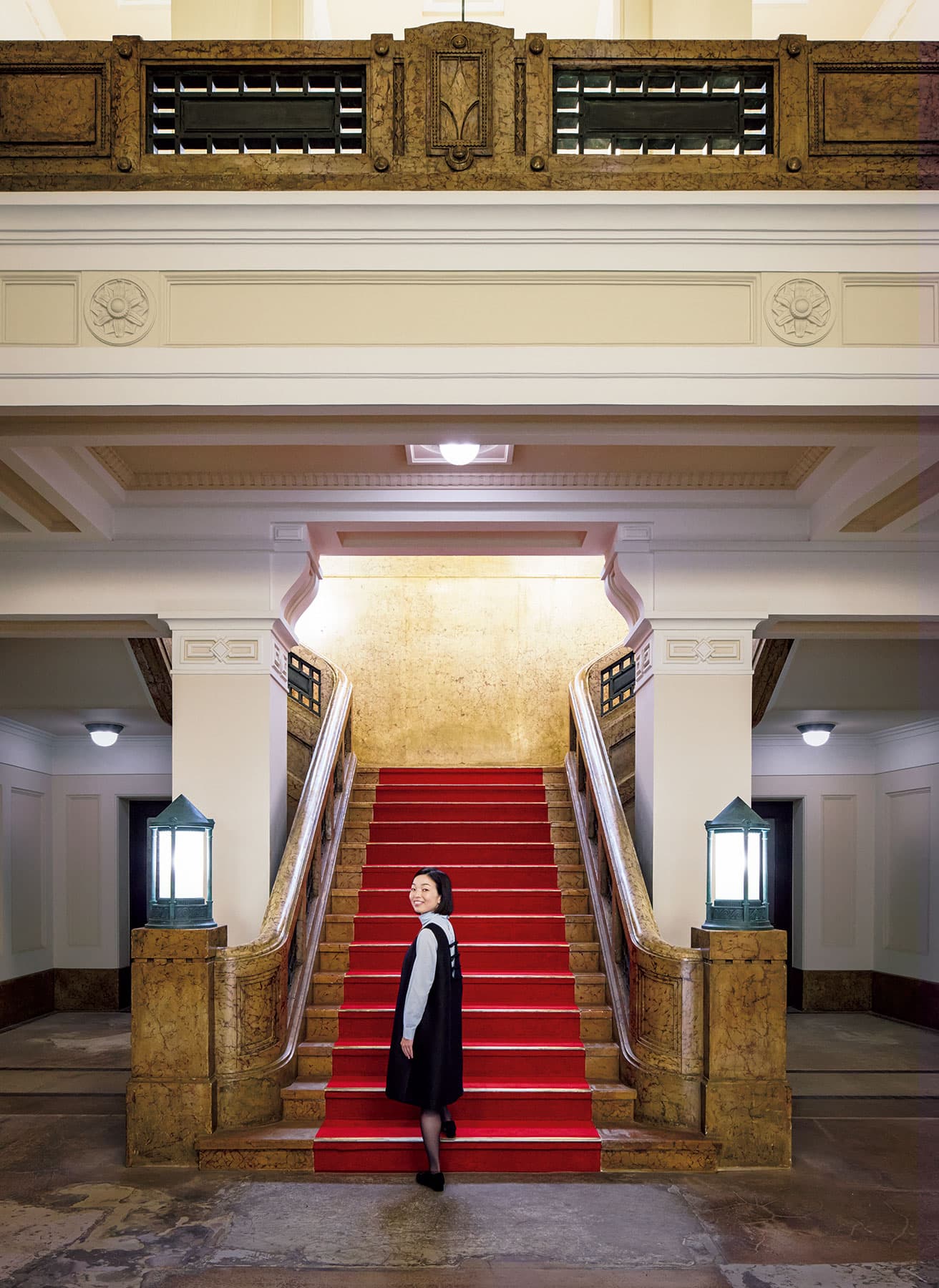 1階階段。RC造でもともと人造大理石塗だったものを塗装で補修した。手すりの飾りは木製メッキ仕上げ。照明は竣工当初からのもの。