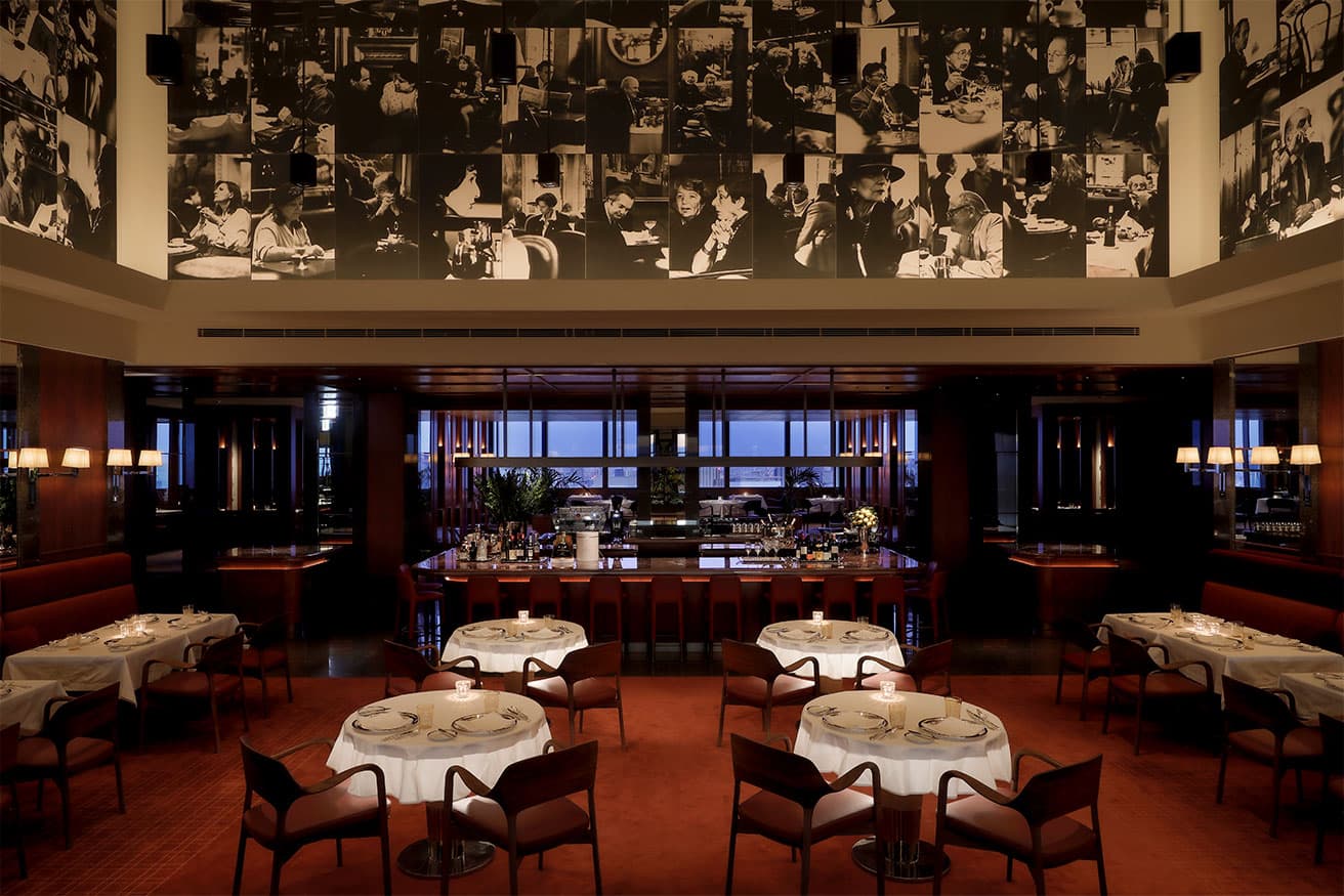 中央にボルドーカラーの大理石のバーカウンターが新設された〈ジランドール  by アラン デュカス〉。照度を落とした店内にラウンドテーブルの光が浮かび上がるのもロマンチックな演出だ。フランス人写真家、ヴェラ・マーサーによる144点のモノクロフォトコラージュは以前のまま。