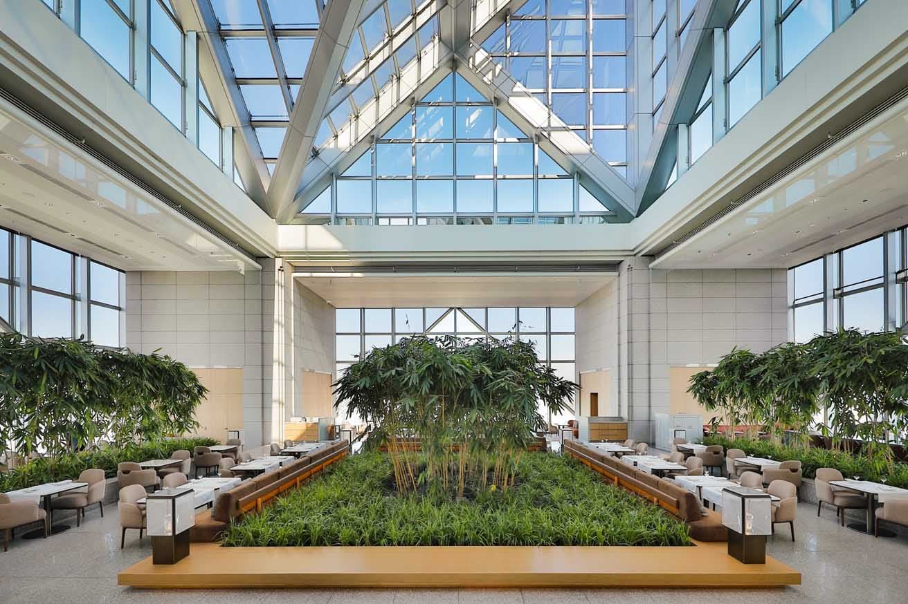 〈新宿パークタワー〉の41階。天井高22mのアトリウムがタイムレスな感動をもたらす。象徴的な竹林はそのままに、〈ピーク ラウンジ〉の家具を一新。「丹下健三の建築がとてもパワフルだから、バランスを取れるよう暖色を選んだ」とジュアン。ベージュとテラコッタの配色、曲線を描く家具のシルエットが柔らかな心地よさを生んでいる。