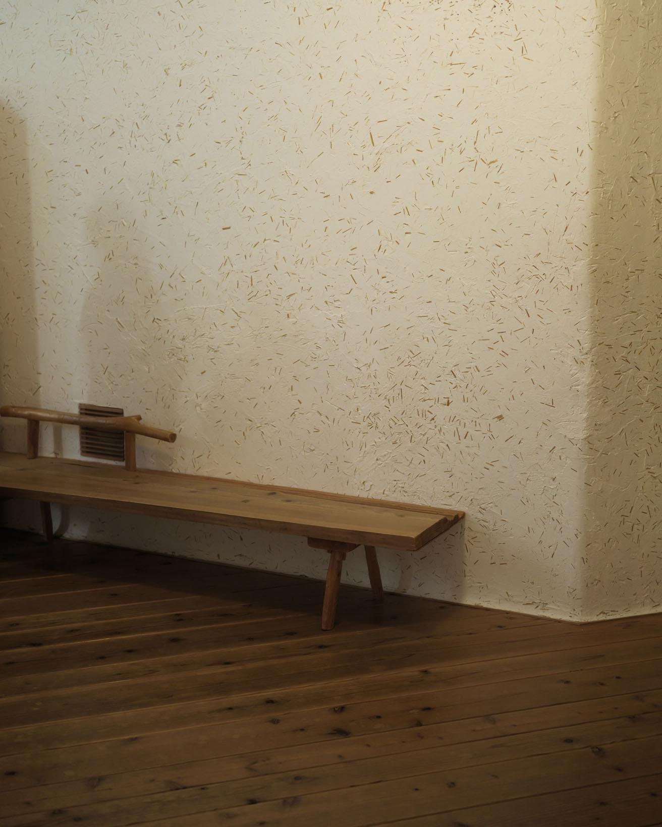 ホールの壁はわら入り漆喰。割りっぱなしの木材で作った椅子は、こちらも「縄文建築団」の作。