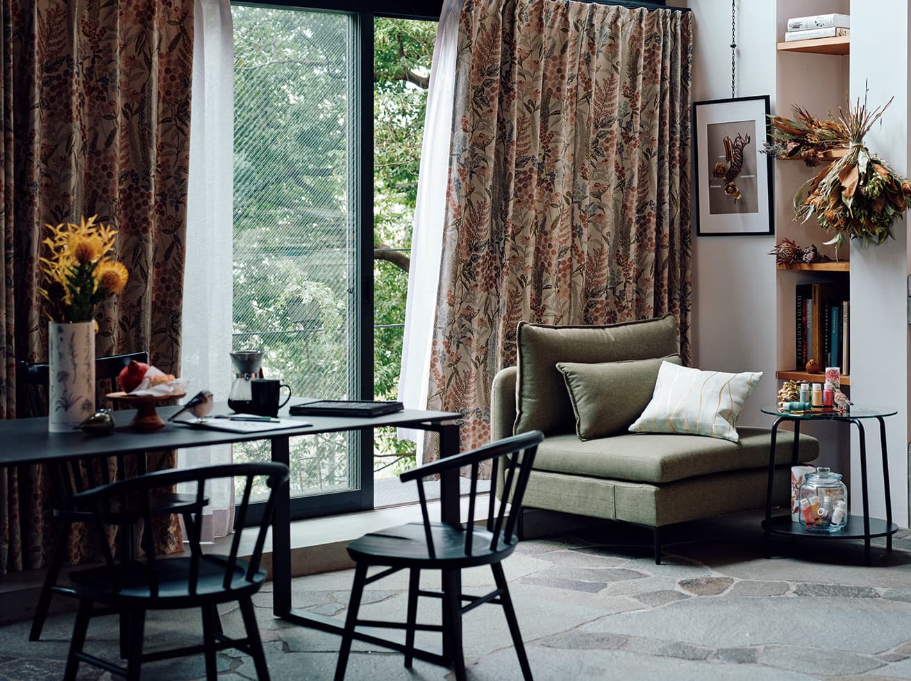 ジャカードカーテンの立体感のある花柄ならば、カーテンがまるで風に揺れる花束となってインテリアの主役になるはず。カーテンとの暮らしがより豊かな時間に。オーダーカーテン1.5倍ヒダ(W176×H213㎝×2枚)30,900円、オーダーレースカーテン2倍ヒダ(W176×H212㎝×2枚)44,000円、ポスターフレームA2 1,990円、1人用ソファ(W88×D98×H84㎝)44,990円、オーダークッションカバー1,490円、サイドテーブル(W54×D54×H54㎝)8,990円、ガラスジャー999円、ダイニングチェア(手前)各25,000円、ダイニングチェア(奥)14,990円、ダイニングテーブル(W150×D90×H70㎝)79,990円、マグ1,290円、ドリッパーセット2,490円(以上ニトリ)。テーブル、ガラスジャーなどの絵画用品、置物、棚の書籍、飾られた植物などはスタイリスト私物。